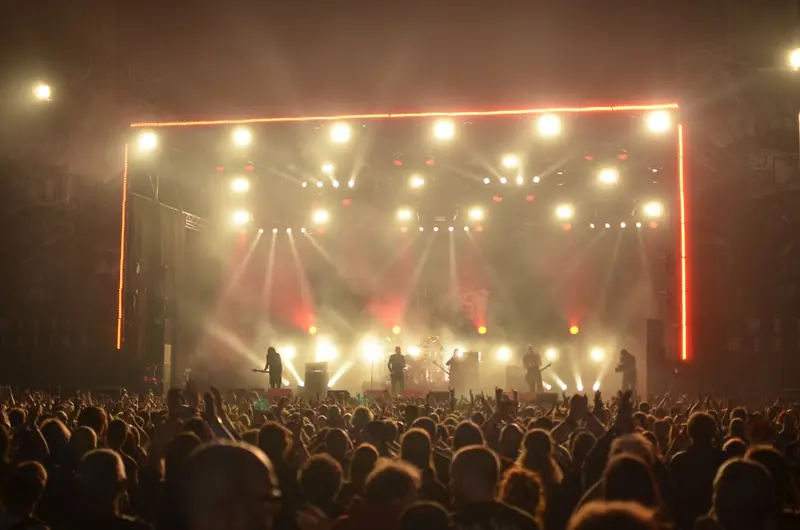 A band silhouetted against a wall of stage lights in front of a huge crowd